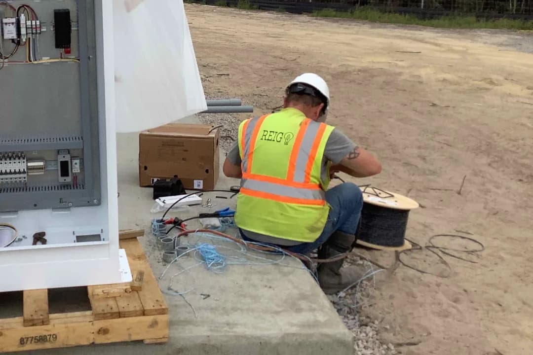 Field technician terminates and tests communications cabling at a PV equipment cabinet as part of site monitoring and controls integration.