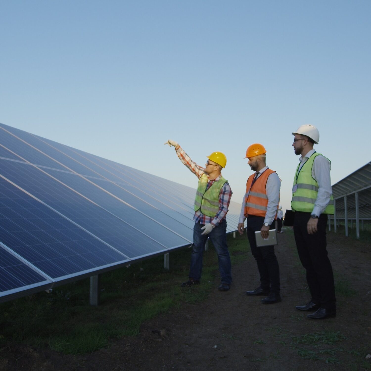 Group of adult men on field with rows of solar panels having professional discussion while working in team